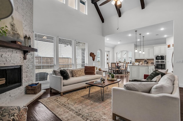 living room with ceiling fan, high vaulted ceiling, a fireplace, wood finished floors, and beam ceiling