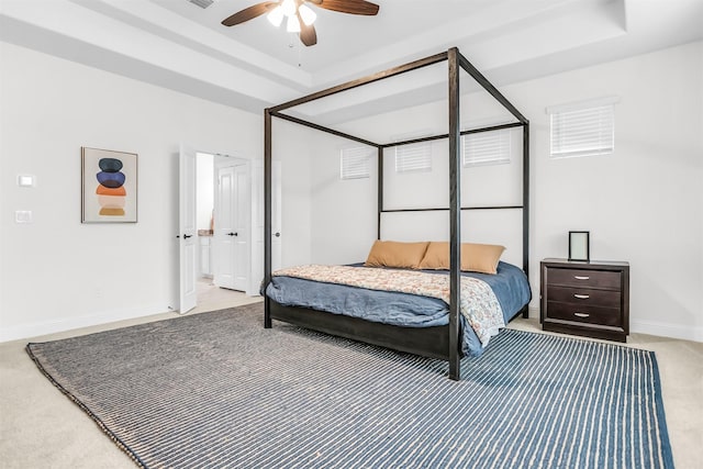 carpeted bedroom featuring a ceiling fan, a tray ceiling, visible vents, and baseboards