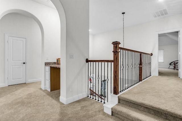 staircase with arched walkways, carpet, visible vents, and baseboards