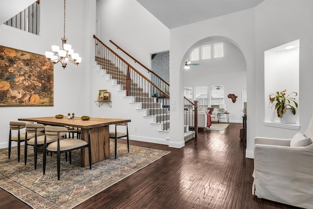 dining area with baseboards, arched walkways, dark wood finished floors, a towering ceiling, and stairway