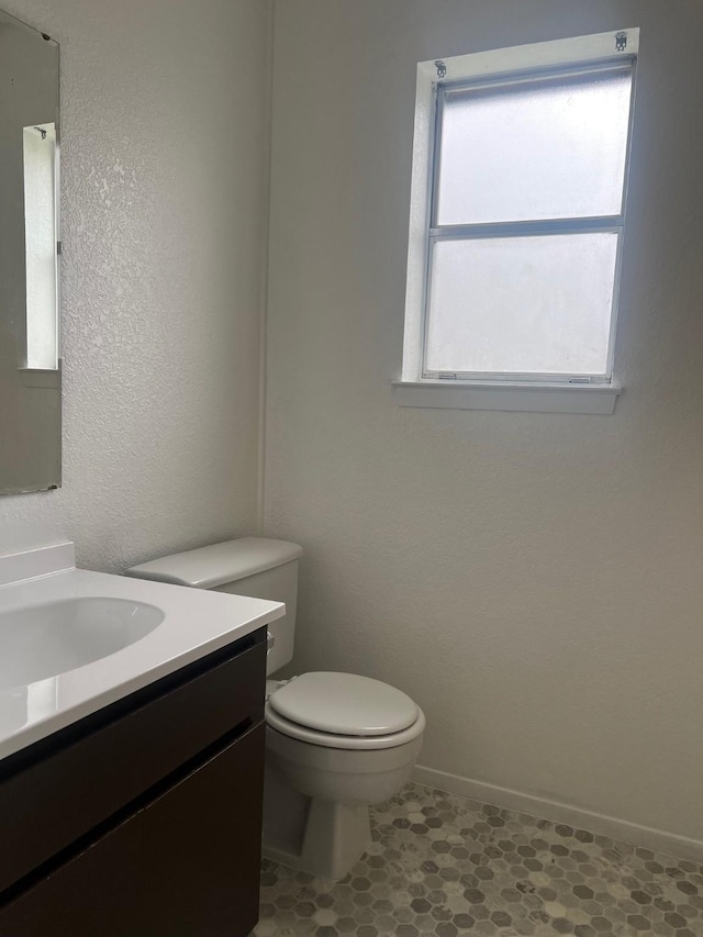 half bath with baseboards, vanity, and toilet