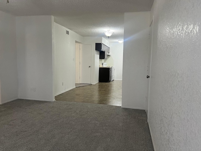 unfurnished room with visible vents, dark colored carpet, and a textured ceiling