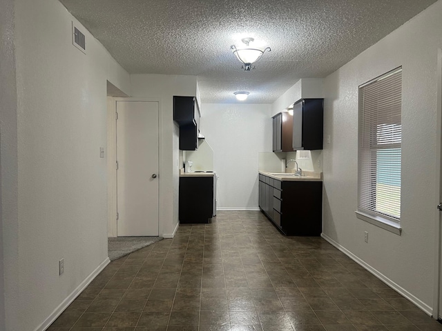 interior space with a textured ceiling, a sink, visible vents, baseboards, and light countertops