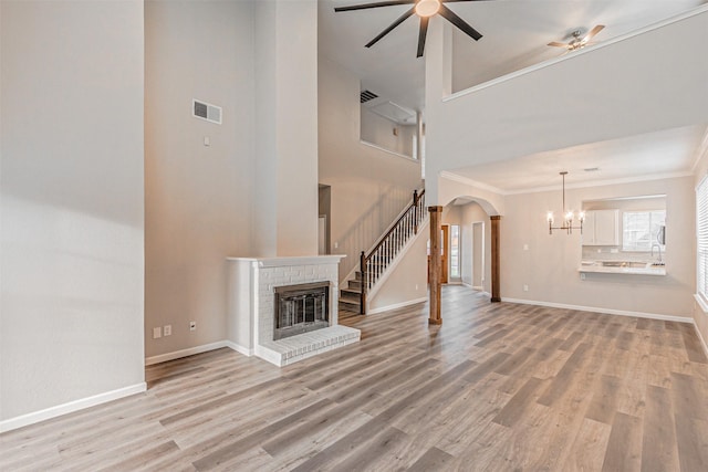 unfurnished living room with light wood finished floors, visible vents, arched walkways, a brick fireplace, and ceiling fan with notable chandelier