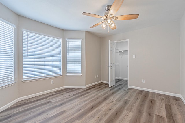 interior space with a ceiling fan, baseboards, a spacious closet, a closet, and light wood finished floors