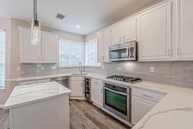 kitchen with stainless steel appliances, a sink, visible vents, white cabinets, and decorative backsplash