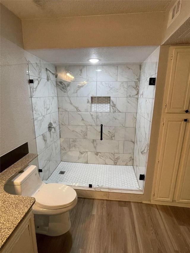 full bathroom featuring wood finished floors, toilet, vanity, a textured ceiling, and a shower stall