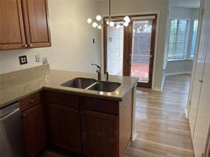 kitchen with wood finished floors, a peninsula, stainless steel dishwasher, and a sink