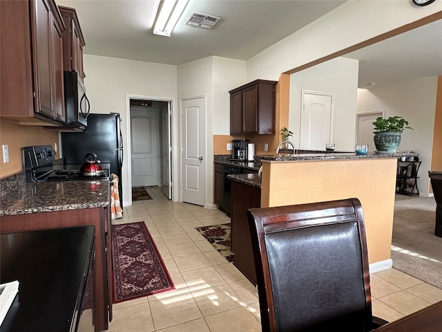 kitchen with light tile patterned floors, visible vents, dark brown cabinetry, a peninsula, and black appliances