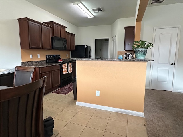 kitchen with dark brown cabinetry, visible vents, dark stone countertops, black appliances, and light tile patterned flooring