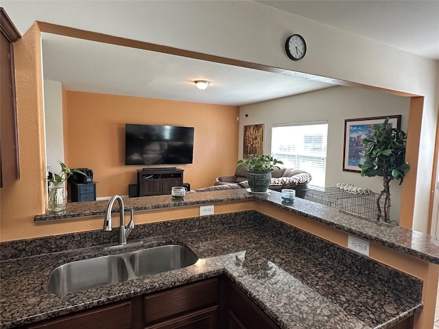 kitchen featuring dark brown cabinets, dark stone counters, open floor plan, and a sink