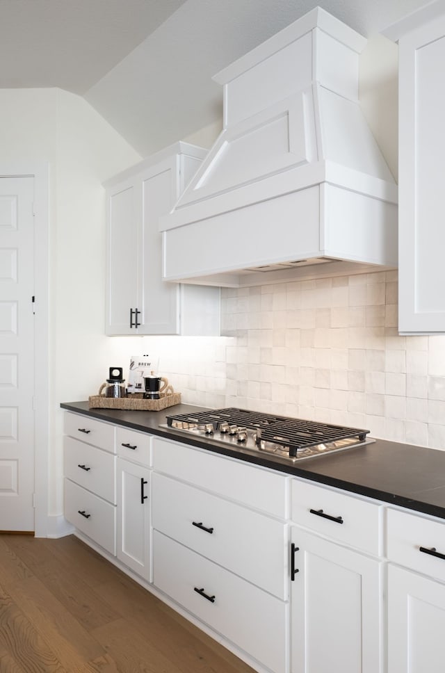 kitchen featuring premium range hood, wood finished floors, backsplash, dark countertops, and stainless steel gas stovetop