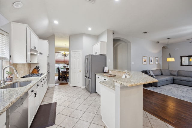 kitchen with stainless steel appliances, open floor plan, a sink, a peninsula, and under cabinet range hood