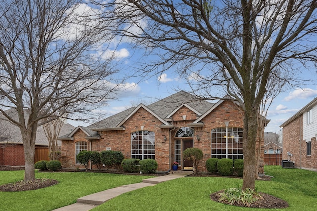 traditional home with a front yard, brick siding, fence, and roof with shingles