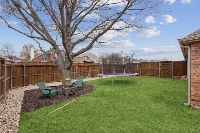 view of yard featuring a fenced backyard, a trampoline, and a fire pit