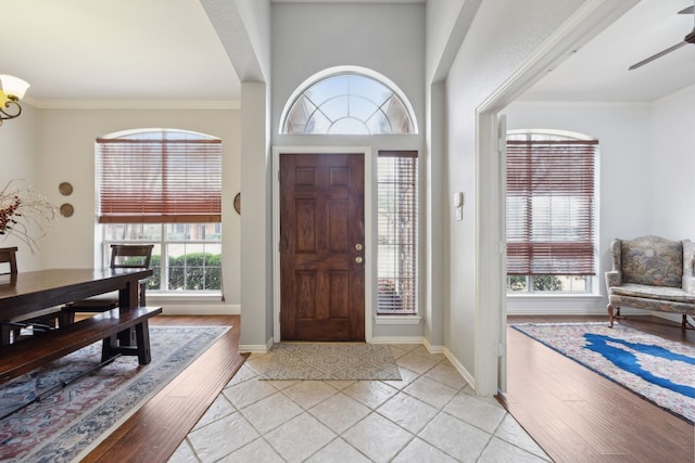 foyer entrance with ornamental molding, light tile patterned floors, baseboards, and ceiling fan with notable chandelier