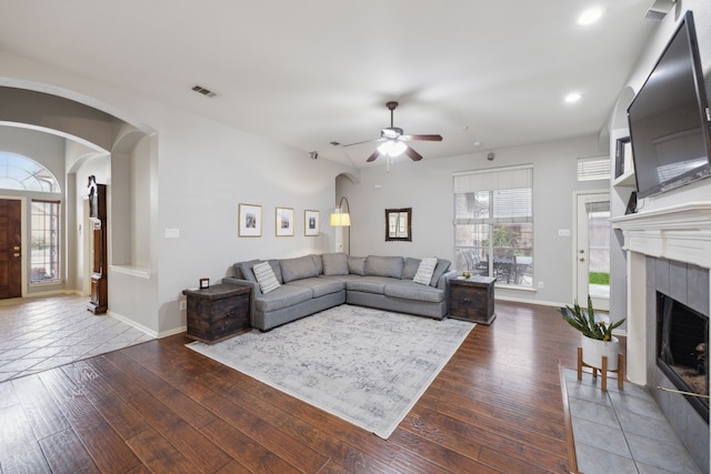 living area featuring arched walkways, a fireplace, wood-type flooring, visible vents, and baseboards