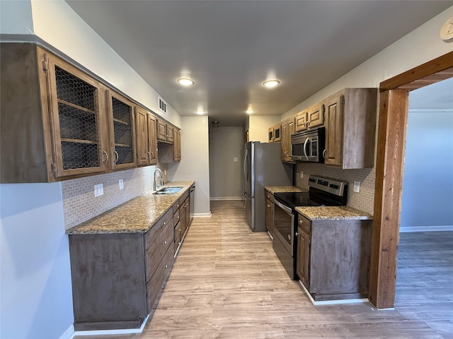 kitchen with visible vents, a sink, glass insert cabinets, appliances with stainless steel finishes, and light wood-type flooring