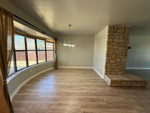 unfurnished dining area featuring a notable chandelier, baseboards, ornate columns, and wood finished floors