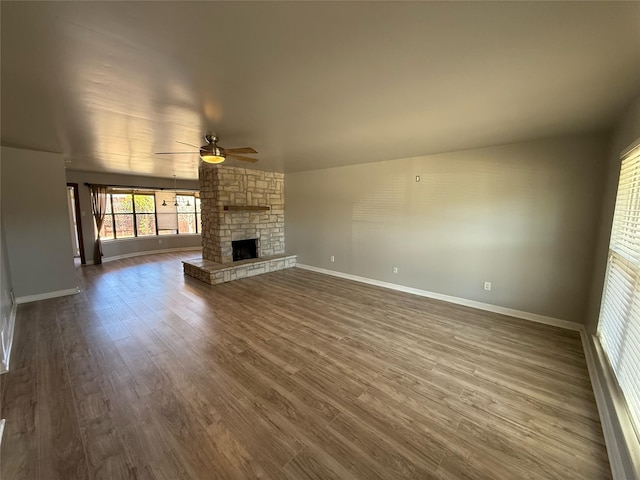 unfurnished living room featuring ceiling fan, baseboards, dark wood-style flooring, and a fireplace