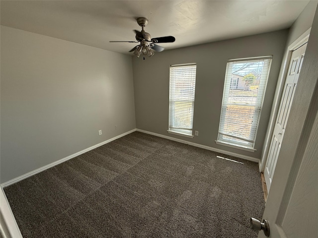 empty room featuring a ceiling fan, baseboards, and dark carpet