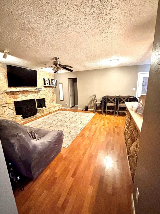 living area with a stone fireplace, a textured ceiling, wood finished floors, and a ceiling fan