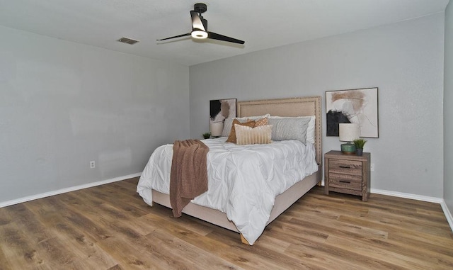 bedroom with a ceiling fan, wood finished floors, visible vents, and baseboards