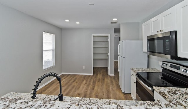 kitchen with stainless steel appliances, light stone countertops, white cabinets, wood finished floors, and baseboards