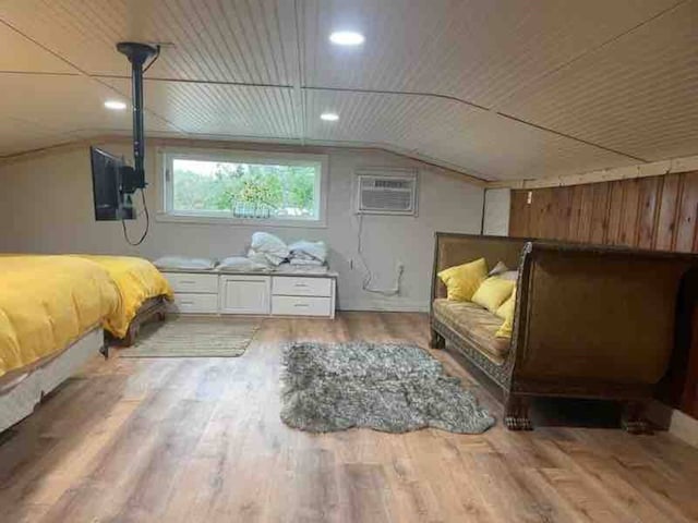 bedroom featuring lofted ceiling, a wall unit AC, wood walls, and wood finished floors