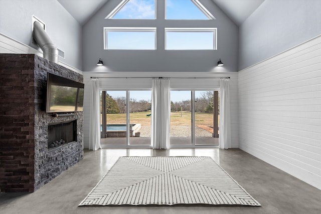 unfurnished living room with high vaulted ceiling, a fireplace, and finished concrete flooring