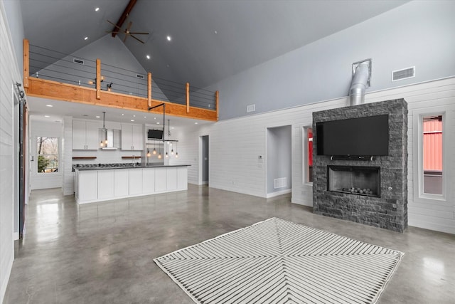 unfurnished living room featuring high vaulted ceiling, a stone fireplace, concrete floors, and visible vents