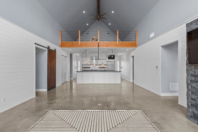 unfurnished living room with finished concrete floors, visible vents, high vaulted ceiling, and a barn door