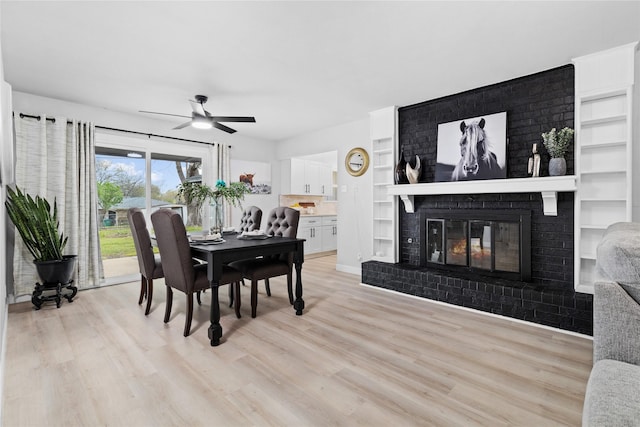 dining room featuring light wood-type flooring, built in features, a ceiling fan, and a brick fireplace