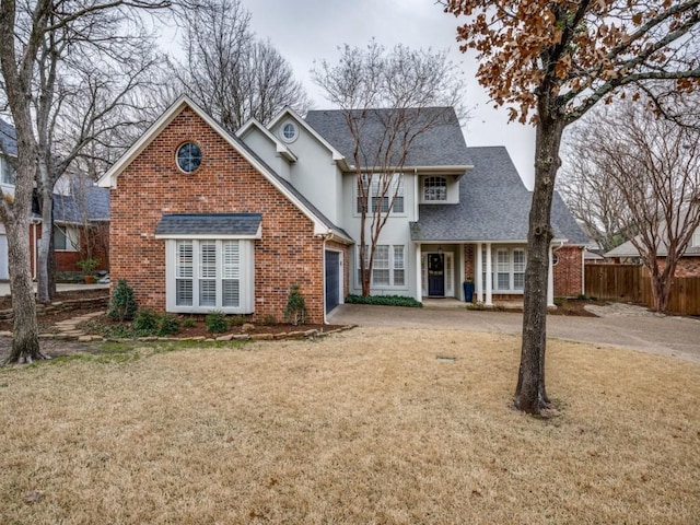 traditional-style home with roof with shingles, brick siding, fence, driveway, and a front lawn