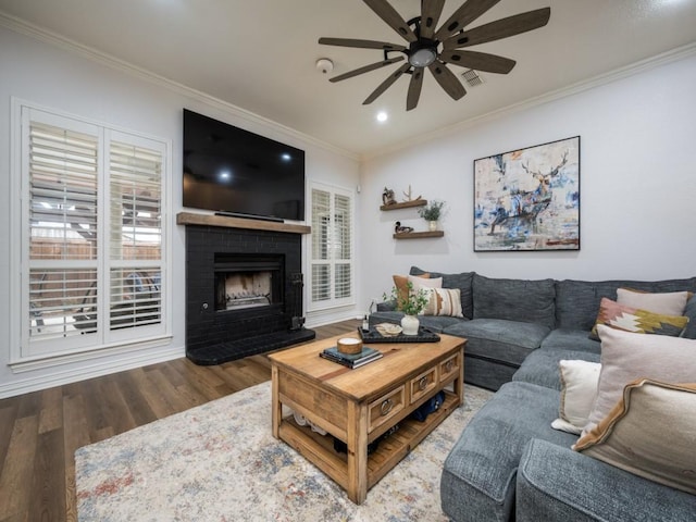 living area with a fireplace, wood finished floors, a ceiling fan, and crown molding