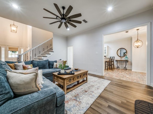 living area with baseboards, stairway, ornamental molding, wood finished floors, and ceiling fan with notable chandelier