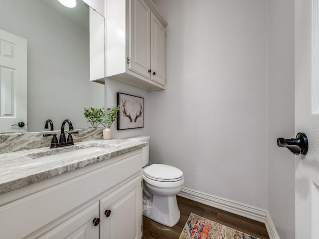 half bath with baseboards, vanity, toilet, and wood finished floors