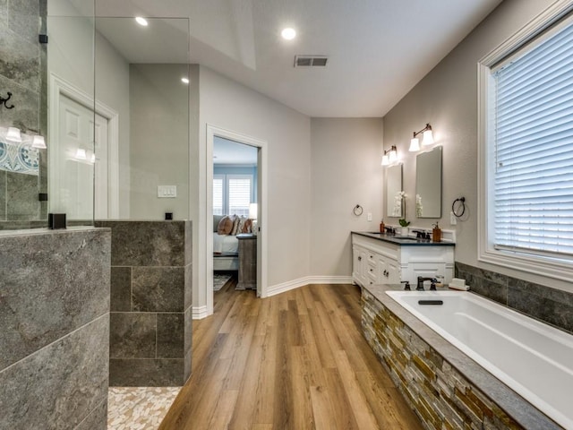 ensuite bathroom featuring a walk in shower, wood finished floors, vanity, visible vents, and ensuite bath