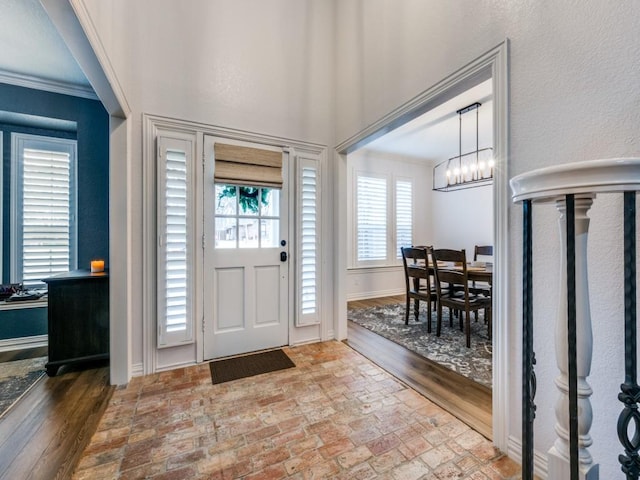 entryway with brick floor, baseboards, a chandelier, and crown molding