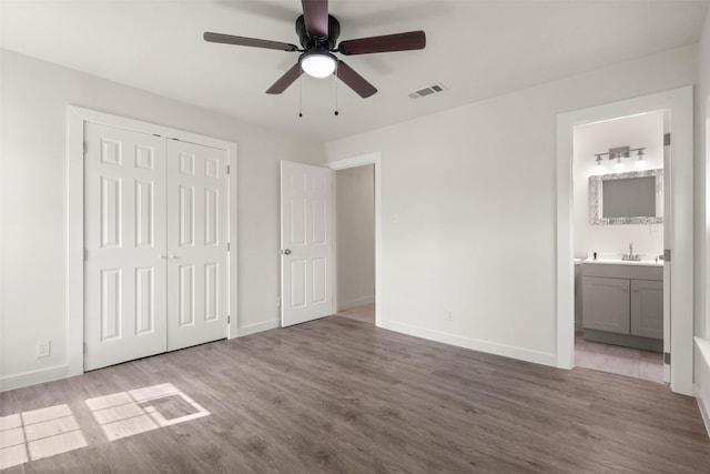 unfurnished bedroom featuring a closet, visible vents, a sink, wood finished floors, and baseboards