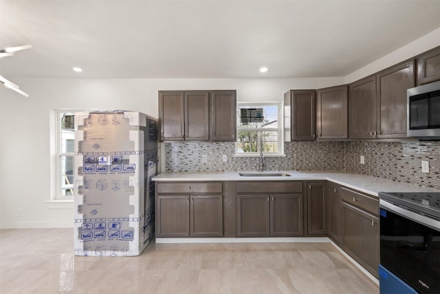 kitchen featuring stainless steel appliances, a sink, dark brown cabinets, light countertops, and backsplash