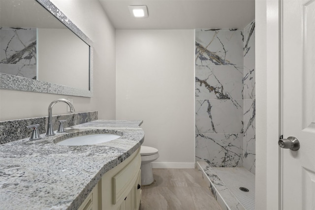 bathroom featuring toilet, a marble finish shower, vanity, and baseboards