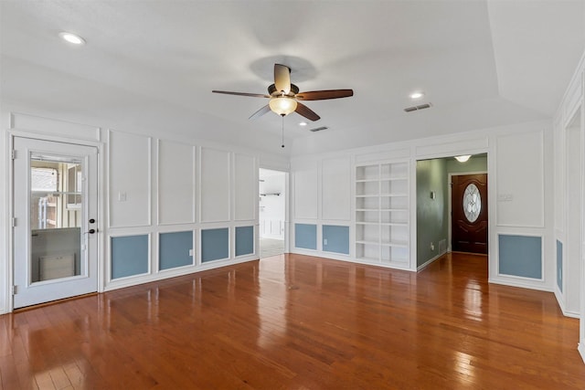 unfurnished living room featuring hardwood / wood-style flooring, visible vents, a decorative wall, and built in features