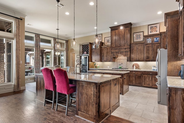 kitchen with arched walkways, visible vents, tasteful backsplash, a center island with sink, and crown molding