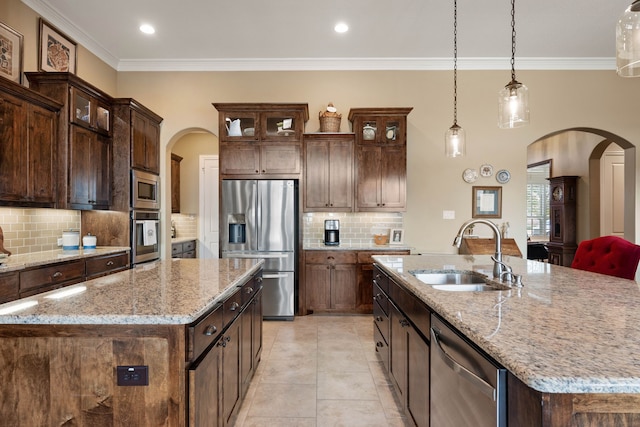 kitchen featuring a kitchen island with sink, arched walkways, stainless steel appliances, and a sink