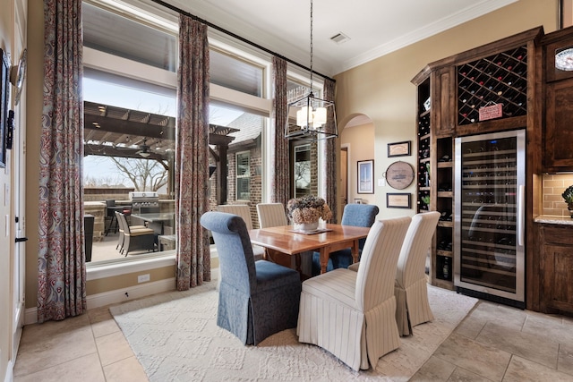 dining room featuring arched walkways, a chandelier, wine cooler, visible vents, and ornamental molding