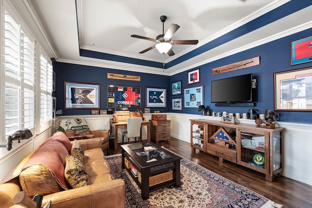 living area with a wainscoted wall, wood finished floors, a ceiling fan, a tray ceiling, and crown molding