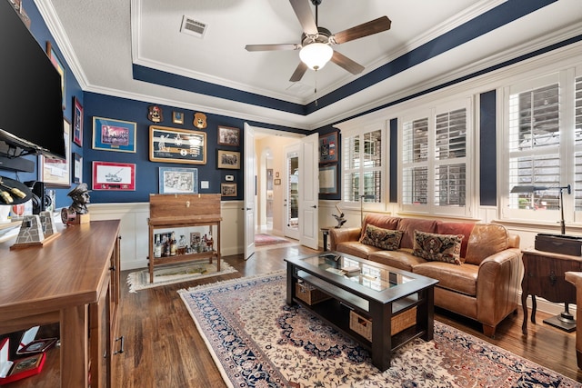 living room featuring visible vents, a raised ceiling, a wainscoted wall, ornamental molding, and wood finished floors