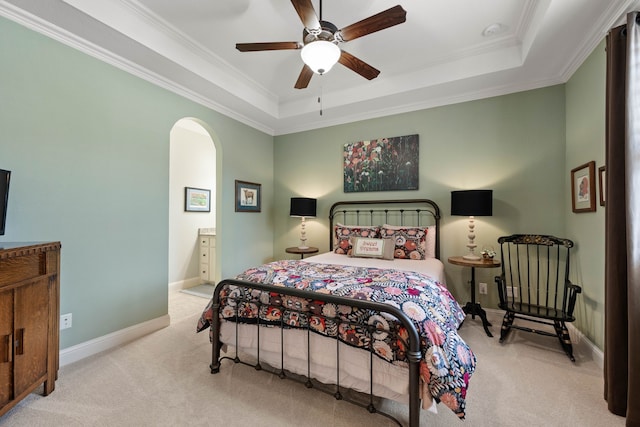 carpeted bedroom with arched walkways, connected bathroom, baseboards, a raised ceiling, and crown molding