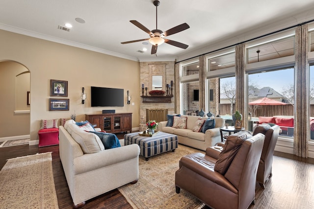 living area with arched walkways, crown molding, visible vents, wood finished floors, and baseboards